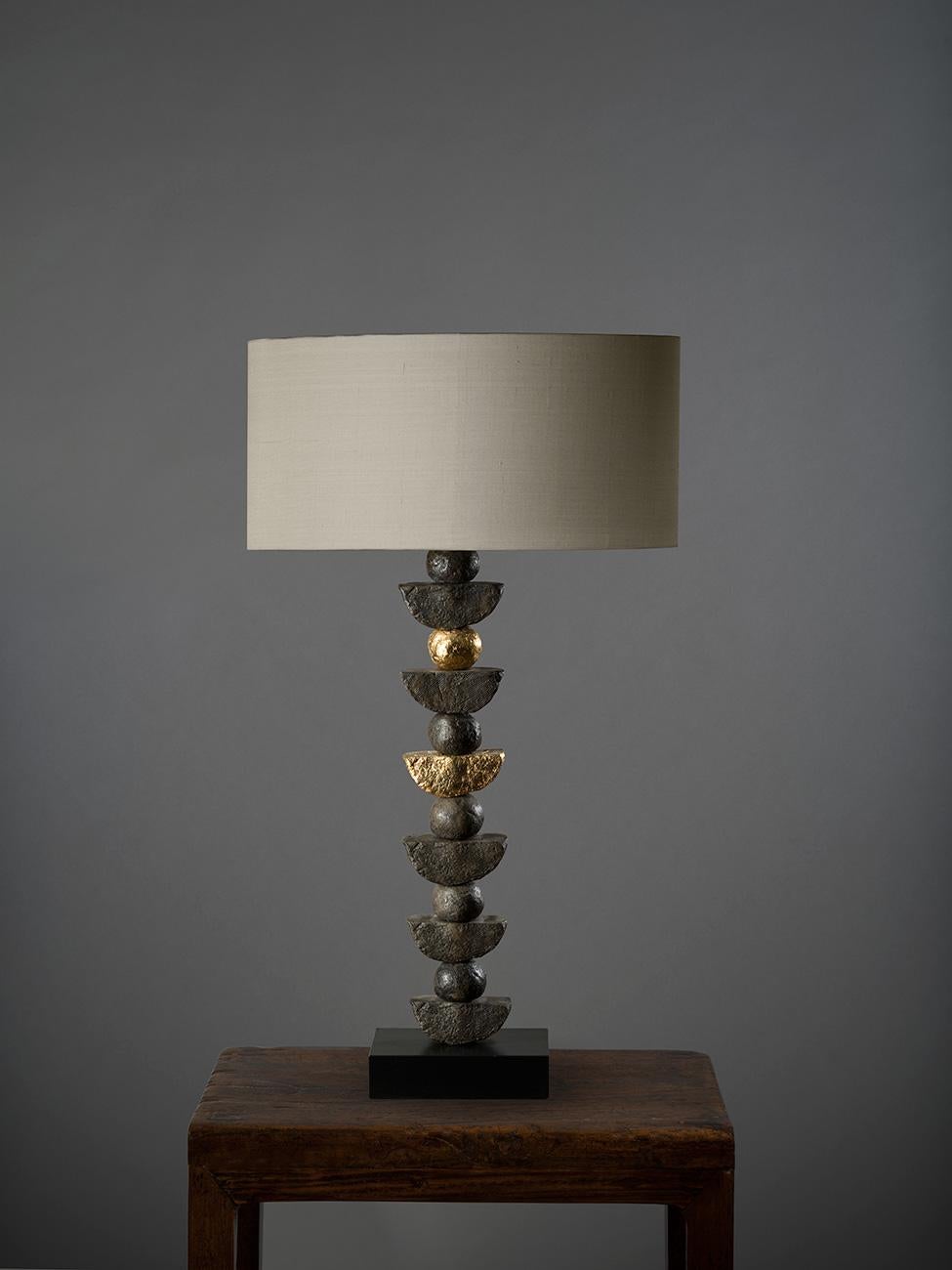 This contemporary Margit Wittig table lamp is mounted on a slate base and features multiple bronze resin handcrafted semi-circles. Each element is hand cast and patinated to increase tonal contrast and enhance the surface texture. The 24-karat gold