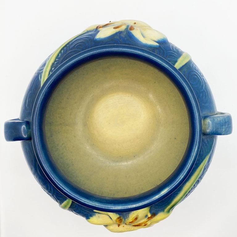 A rich blue ceramic jardiniere decorated with cream lilies. This planter by Roseville was created in 1946 and is in the Zephyr Lily pattern in Bermuda Blue. This particular pattern is a rare find in this condition. It features a handle on each side.