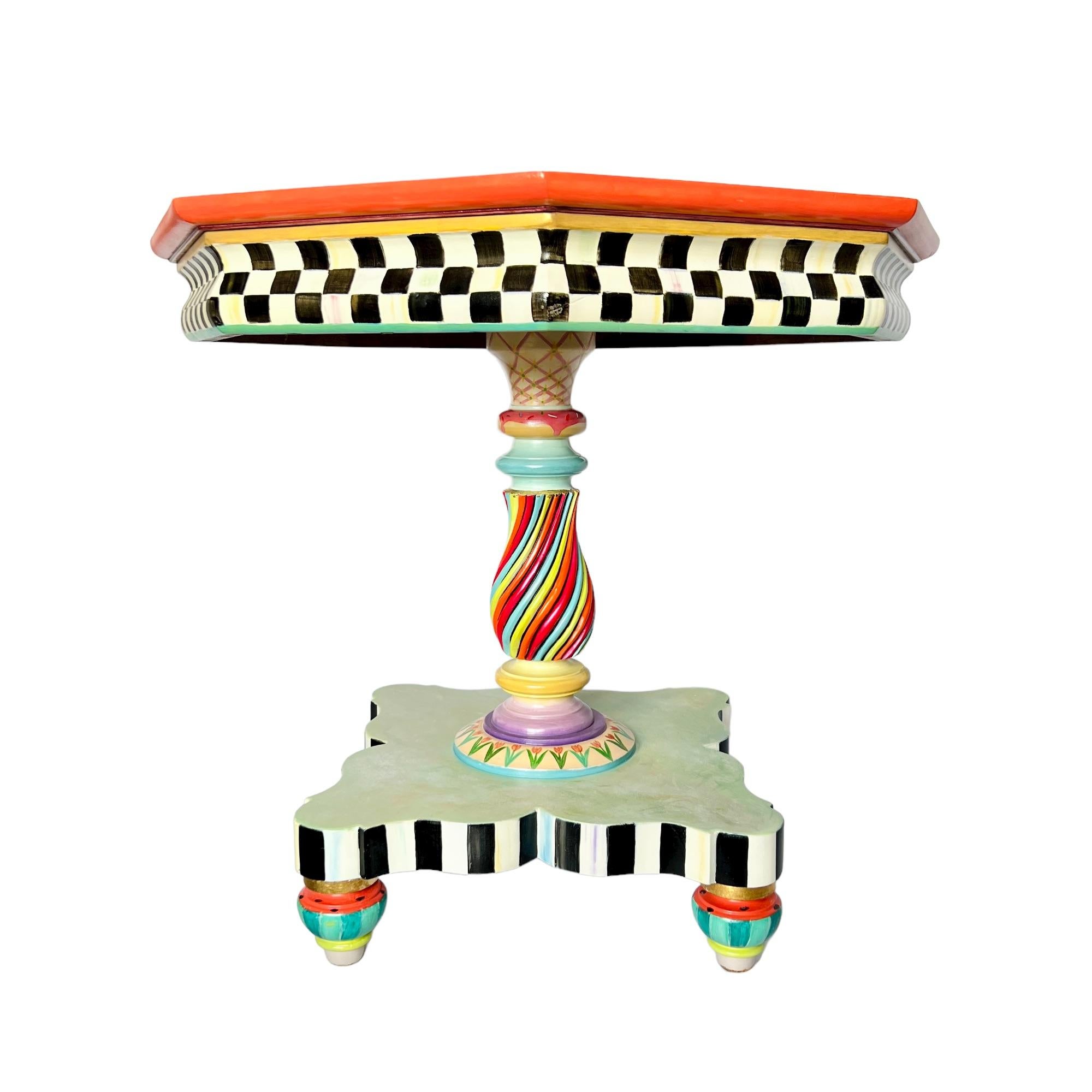 Vibrant and whimsical, this finely detailed turned wood octagon pedestal accent table has been given a one-of-a-kind hand painted update in the manner of MacKenzie-Childs. The pearly cream top features a geometric yellow, pink, green and blue flower