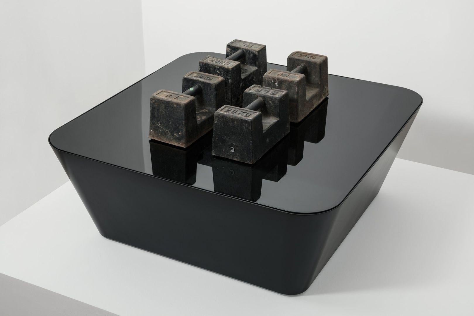 La table Zero-In crée une illusion d'apesanteur, avec des parois inclinées sans soudure à des angles inattendus, surmontées d'une surface en verre, le tout soutenu par des pieds cachés qui créent une zone d'ombre sous la structure.

Construite à