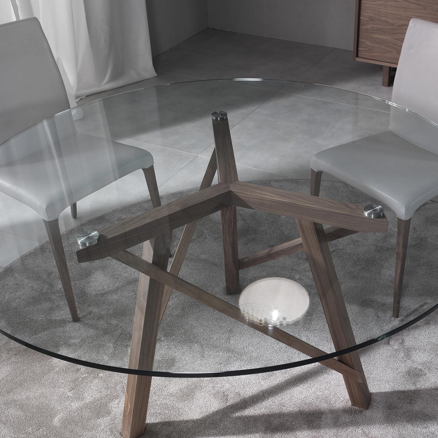 Conçue par Giuliano et Gabriele Cappelletti, cette table de salle à manger ronde fait partie de la collection Zeus. Le plateau en verre transparent permet une vue complète de la structure dynamique étonnante en noyer Canaletto qui comprend trois