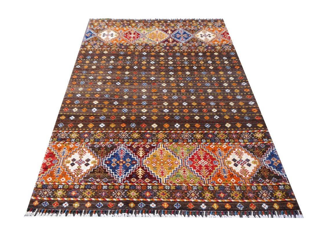 This beautiful almost 5  x 7 ft hand-knotted Arijana Khorjin rug has a brown background and a geometric design in Red, Gold, Green and Blue. 
Production method: hand-knotted
Design: Khorjin Ziegler Arijana
Color: Brown, Green, Goldm Red,