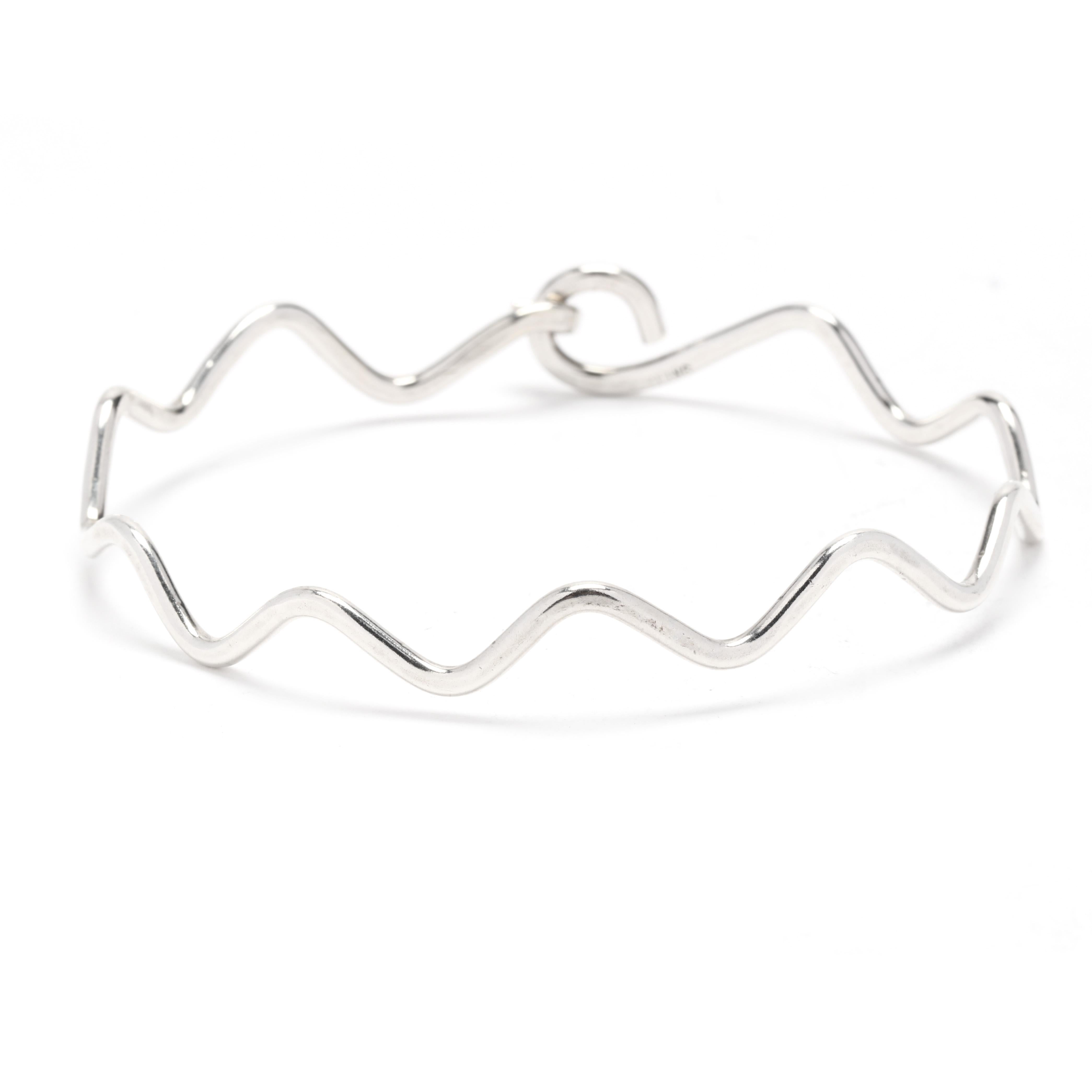 A vintage sterling silver Zig-Zag design bangle bracelet. This bracelet features an undulating zig-zag pattern with an integrated hook and eye closure. It is stamped Sterling. 

Length: 7.25 inch interior circumference

Width: 3/8 inch

Weight: 5.3