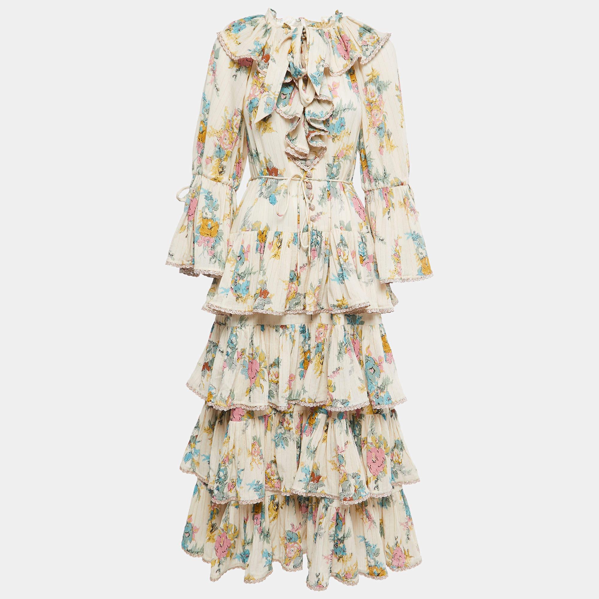 The Zimmermann dress is a charming and elegant piece featuring a cream-colored cotton fabric adorned with intricate floral patterns. Its tiered design adds a playful touch, making it a perfect choice for a stylish summer outfit.

