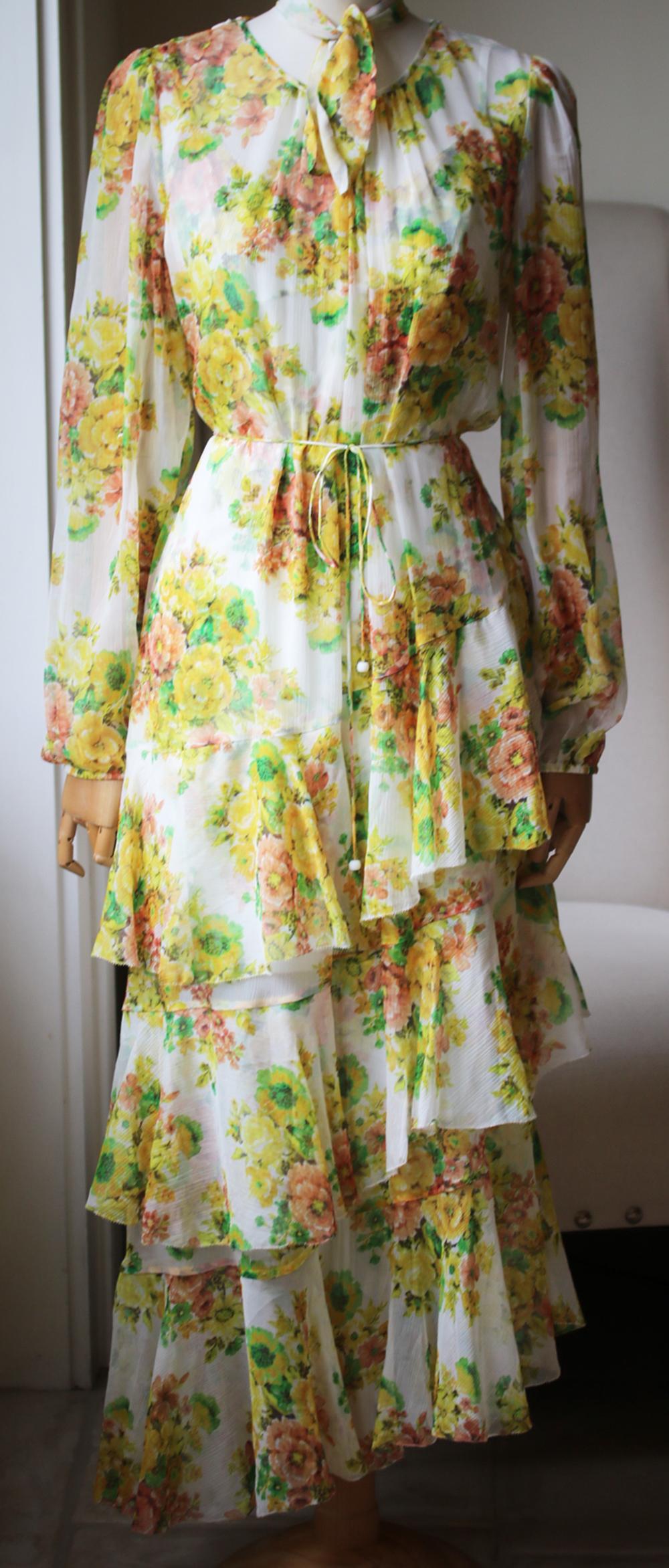 This yellow Zimmermann Golden tiered ruffle floral print midi dress features a round neck with a detachable neck tie, long blouson sleeves, a Citrus Stamp Floral print, an asymmetric ruffle tiered skirt, waist tie and printed slip dress. 100% Silk.
