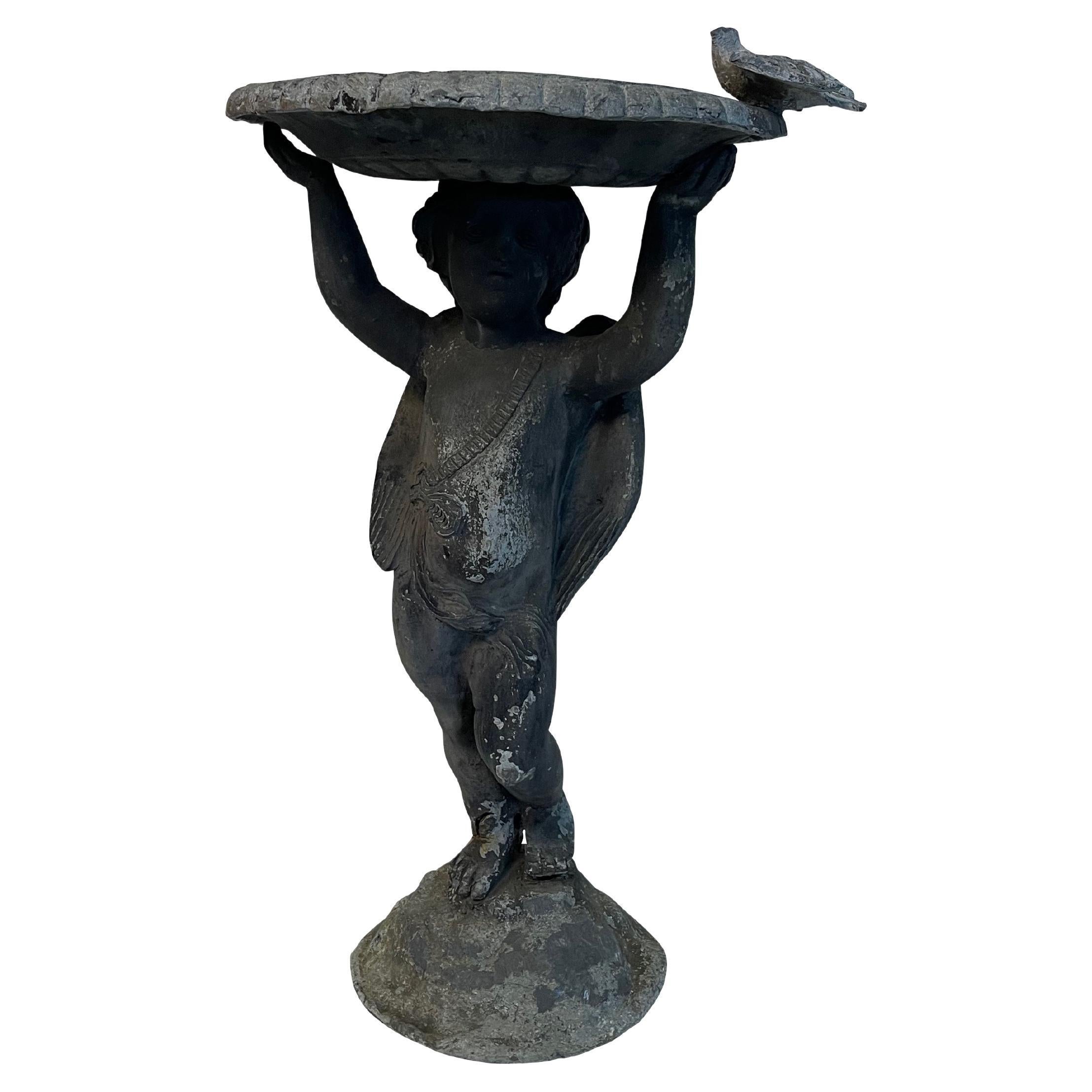English lead birdbath in a small size. Beautifully detailed figural base with a small winged cherub or putti with garland decoration holding a basin above his head. The basin has a reticulated center with a braided edge and the most perfect petite