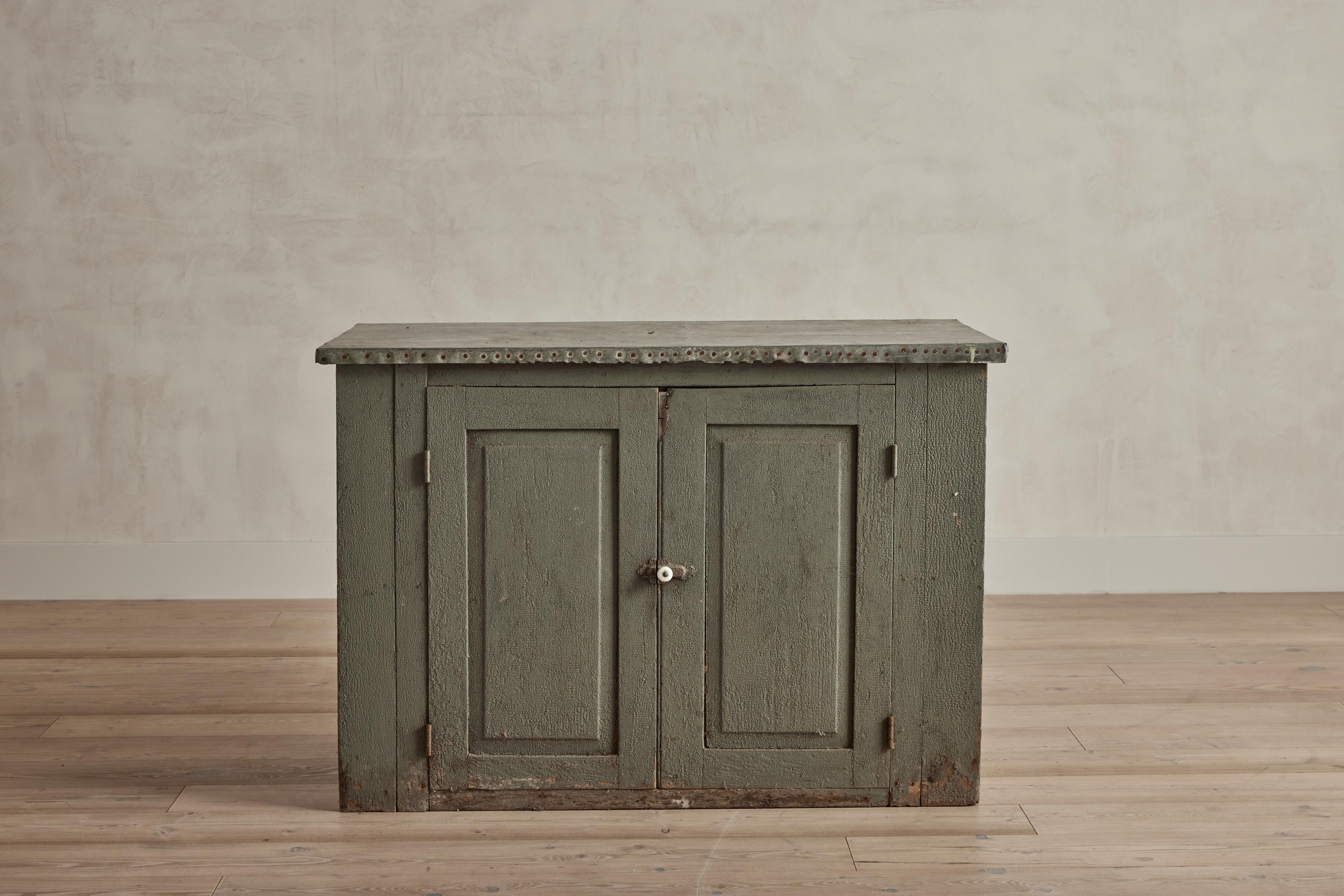 Gray painted two door cabinet with rustic zinc metal door. Visible wear throughout that is consistent with age and use. United States circa 1900.