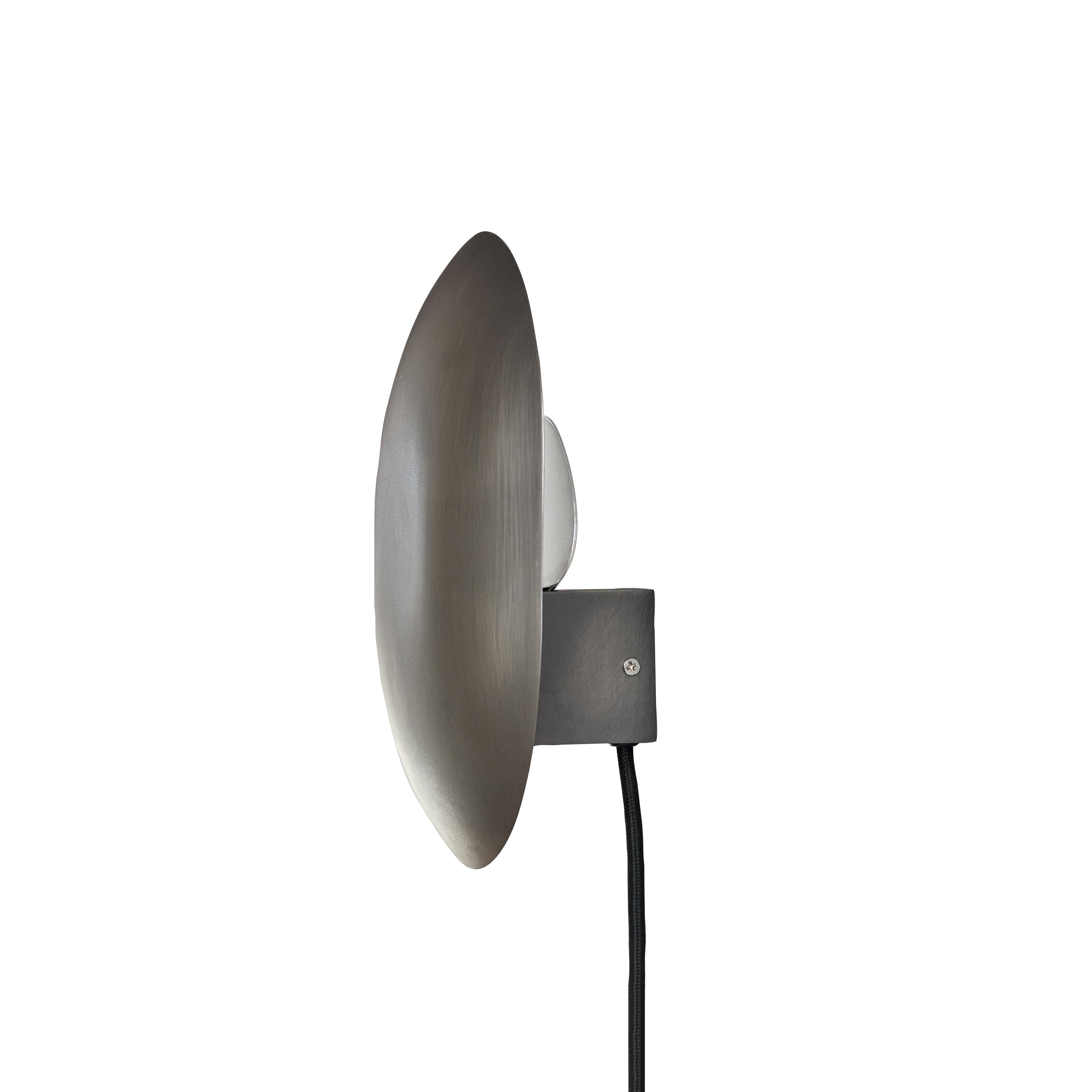 Zink clam wall lamp by 101 Copenhagen
Designed by Kristian Sofus Hansen & Tommy Hyldahl
Dimensions: L 14 x W 22 x H 26 cm
Cable length: 170 cm

Materials: metal: plated metal / zink
Cable: fabric covered cable / black

Characterized by its