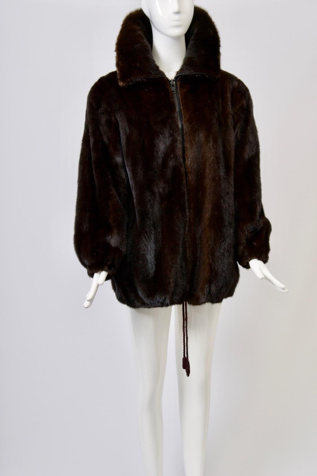 Dark mink hip-length jacket featuring a zippered closure and drawstring hem. The attractive large collar can be worn open or rolled over and fastened for further warmth. Approximate size M.