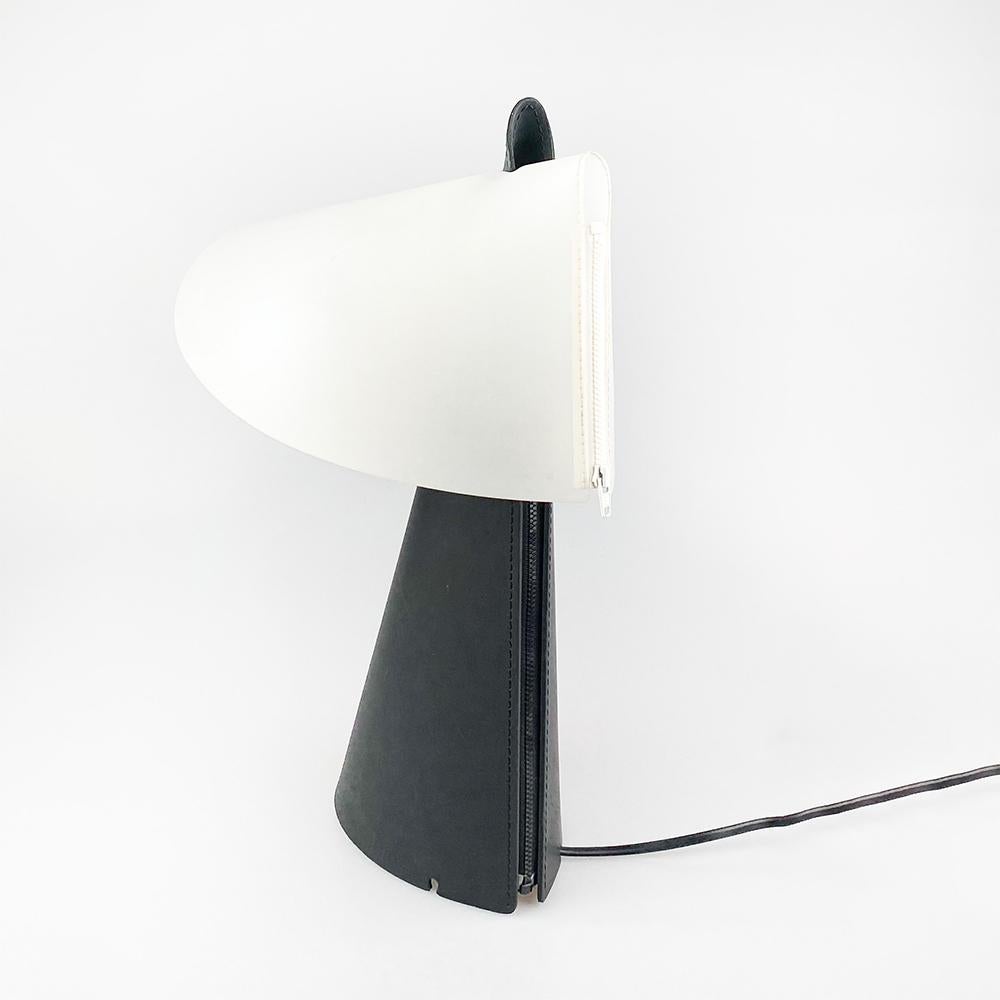 Zip table lamp designed by Sigmar Willnauer for Naos, 1994.

The base is made of Florentine leather with a zipper that runs from the top to the bottom. 

The screen is made of polyester, it also closes with a zipper.

Measurements: 42x37x25 cm.