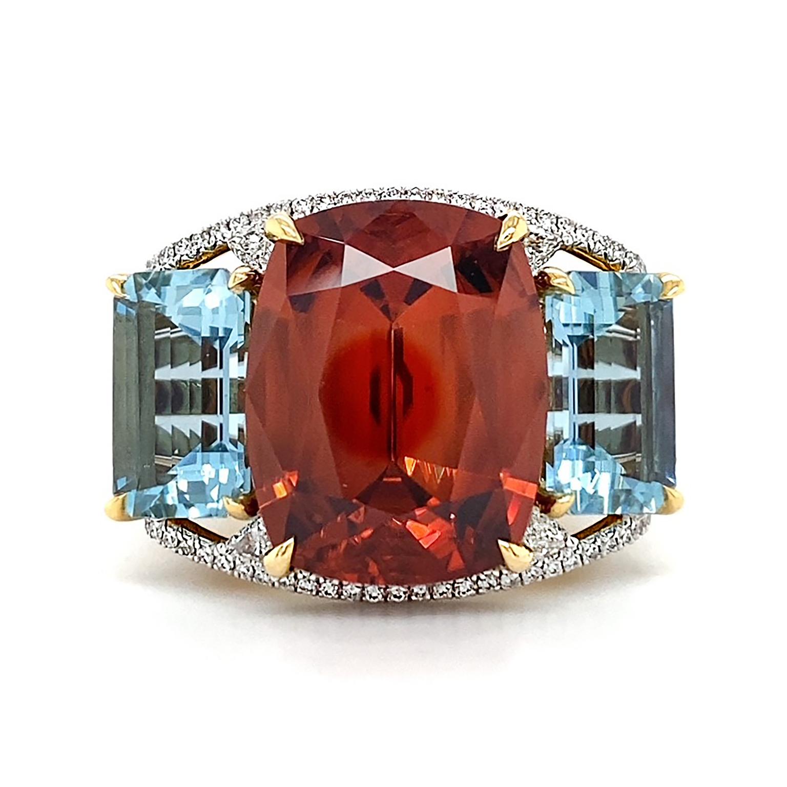 An arresting duo of jewels glow each other. The blazing orange hue of zircon in a cushion cut serves as the culmination of this ring held by 18k yellow gold prongs in the center. More light dances off an emerald cut of aquamarine on each side of the