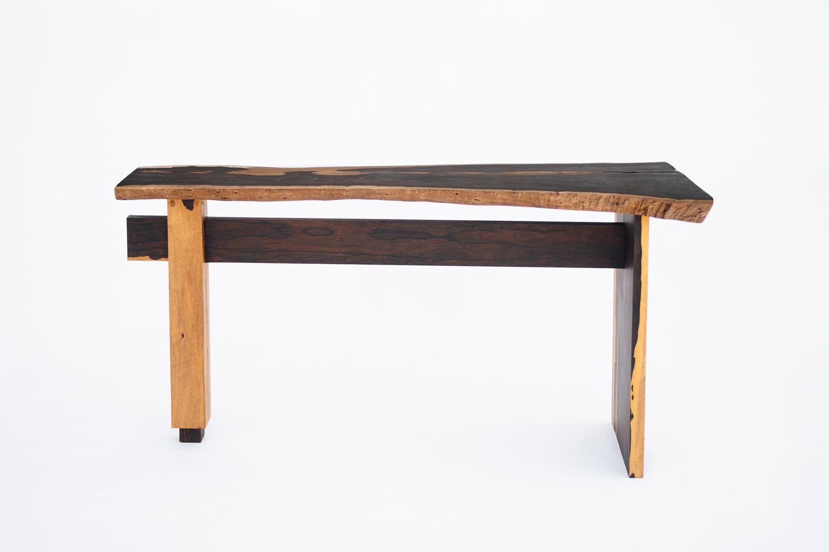 Une table méticuleusement conçue qui met en valeur la beauté naturelle du Ziricote, l'une des essences de bois les plus exquises au monde.
Cette pièce unique peut être utilisée comme bureau ou table d'appoint. Son plateau, plus large à une extrémité
