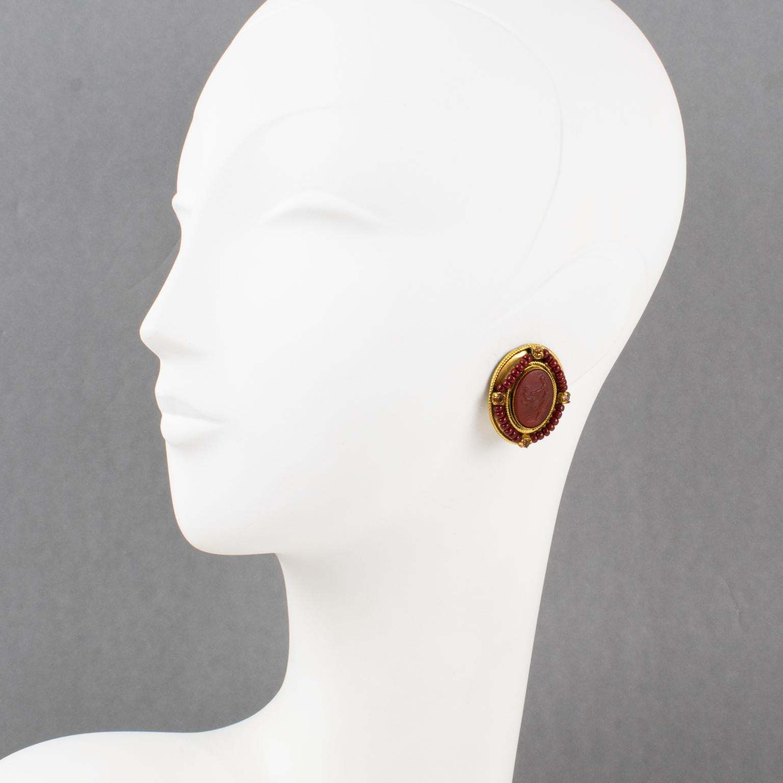 These thrilling Zoe Coste for Reminiscence gilt metal clip-on earrings feature gorgeous Victorian-style poured glass cameos mounted on an oval gilded metal framing and adorned with carnelian red seed beads and yellow topaz crystal rhinestones. The