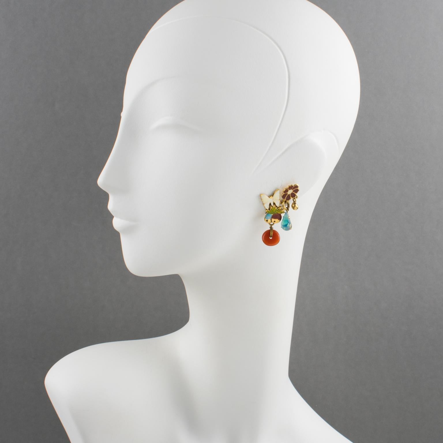 Zoe Coste Paris hat diese hübschen baumelnden Ohrclips entworfen. Die Komposition besteht aus vergoldeten Metallblumen, Schmetterlingen und Früchten, die mit weißer, roter und grüner Emaille verziert sind. Die Ohrringe sind mit baumelnden blauen