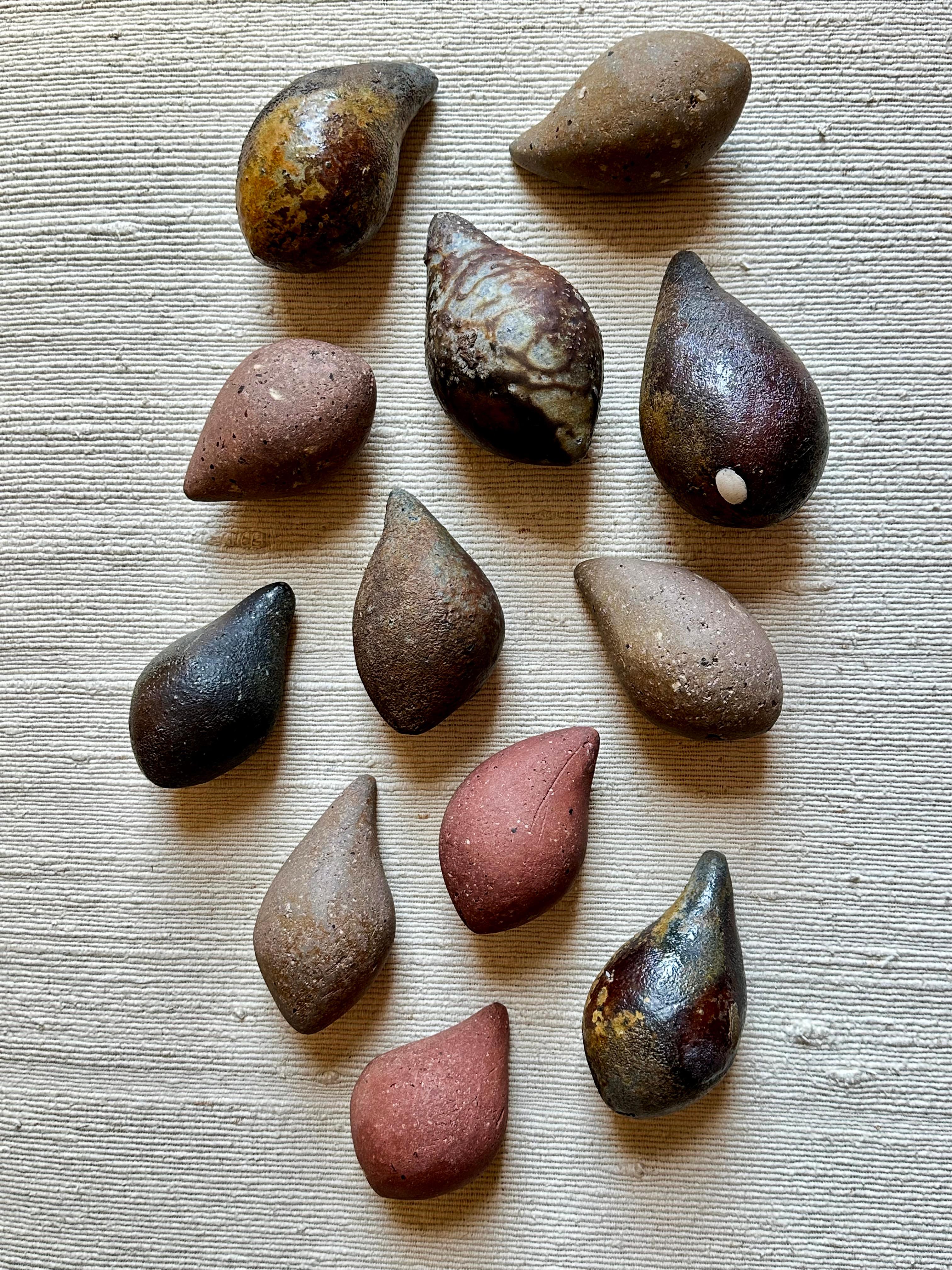 A collection of twelve (12) pod form sculptures made from various stoneware clays hand-collected by the artist in California and Minnesota. Surfaces vary: some are hand-polished to a matte finish, others are wood-fired for four or more days to