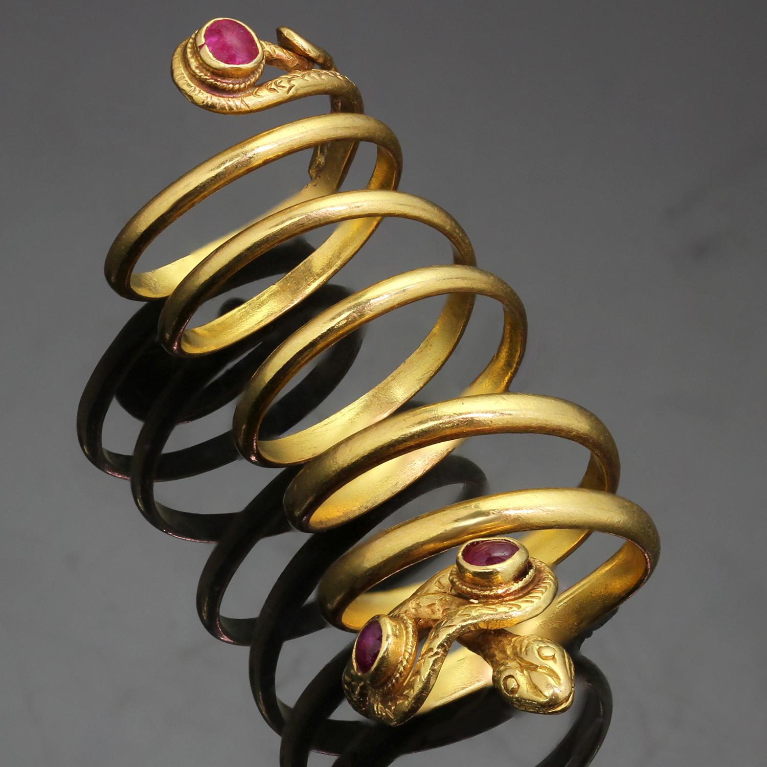 Dieser wunderschöne Vintage-Ring von Zolotas im Stil des Archaeological Revival zeigt ein zeitloses, gewundenes Schlangendesign, das aufwändig in 22 Karat Gelbgold gefertigt und mit einem Paar Cabochon-Rubinen eingefasst ist. Hergestellt in