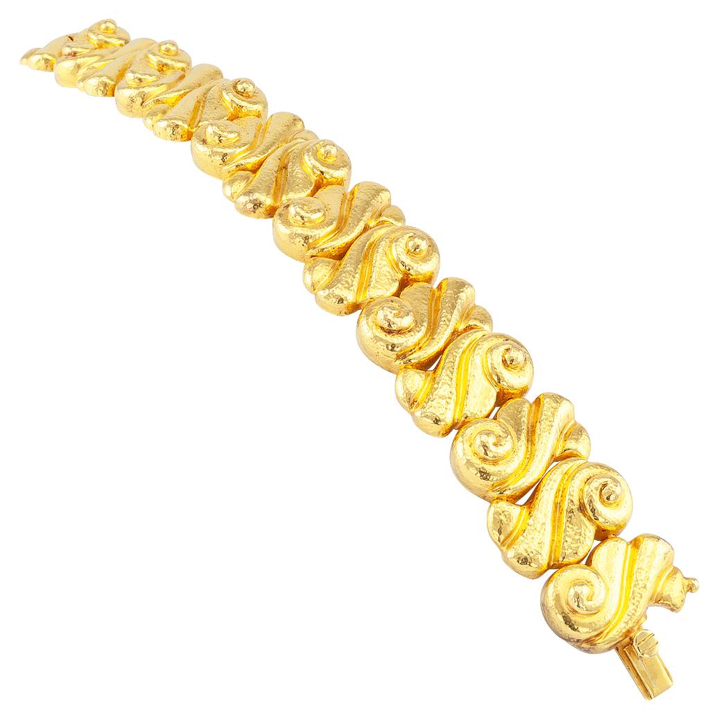 Zolotas 22 karat gold bracelet circa 1980. Comprising a course of complimentary S-shaped links decorated with deeply grooved scrolling motifs and a soft hammered texture to help capture that inimitable glow of 22-karat gold. Very pristine condition