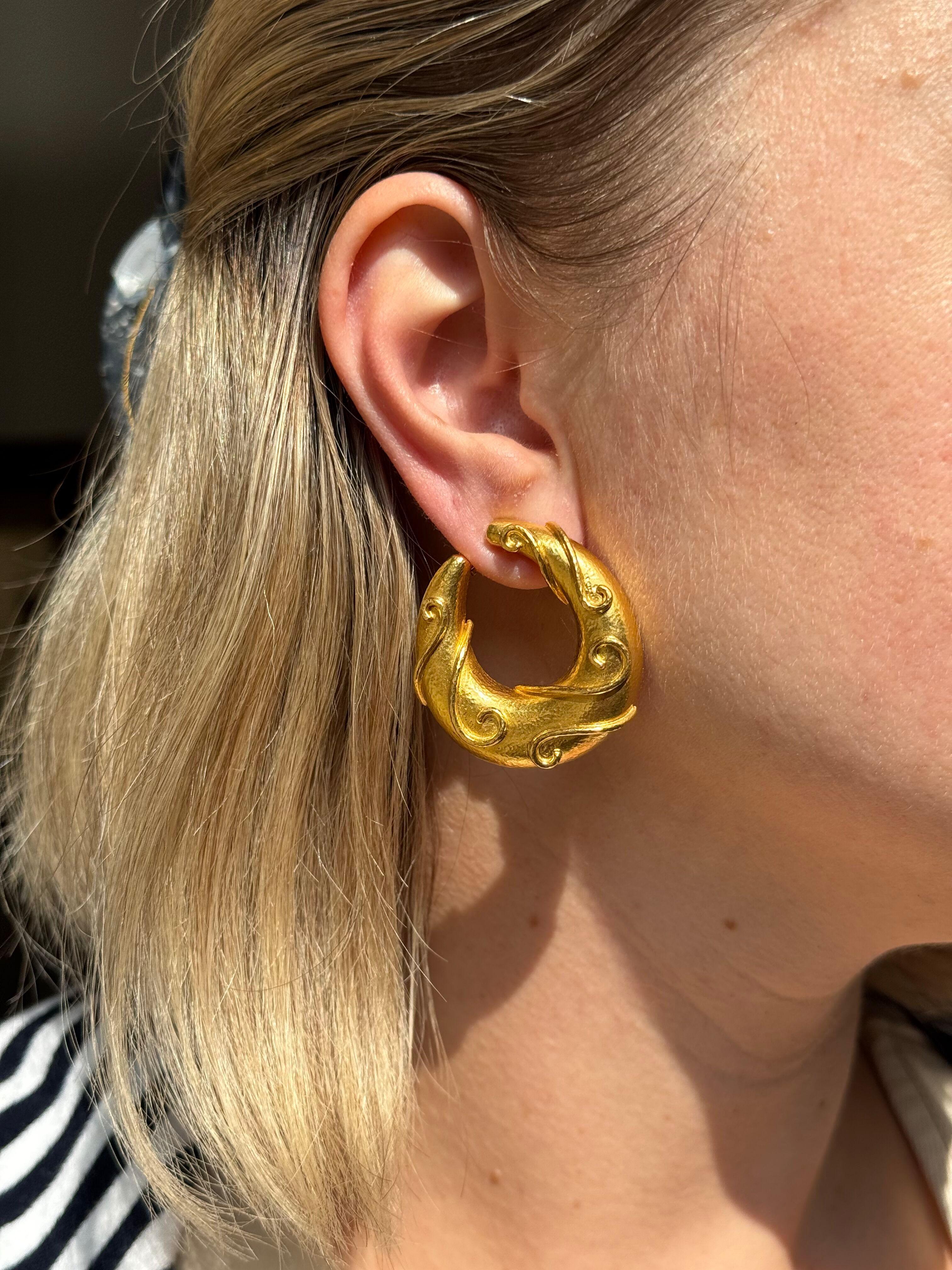 Coppia di orecchini a cerchio in oro giallo 22k di Zolotas, in Grecia, con design a volute.

Gli orecchini misurano 1,5