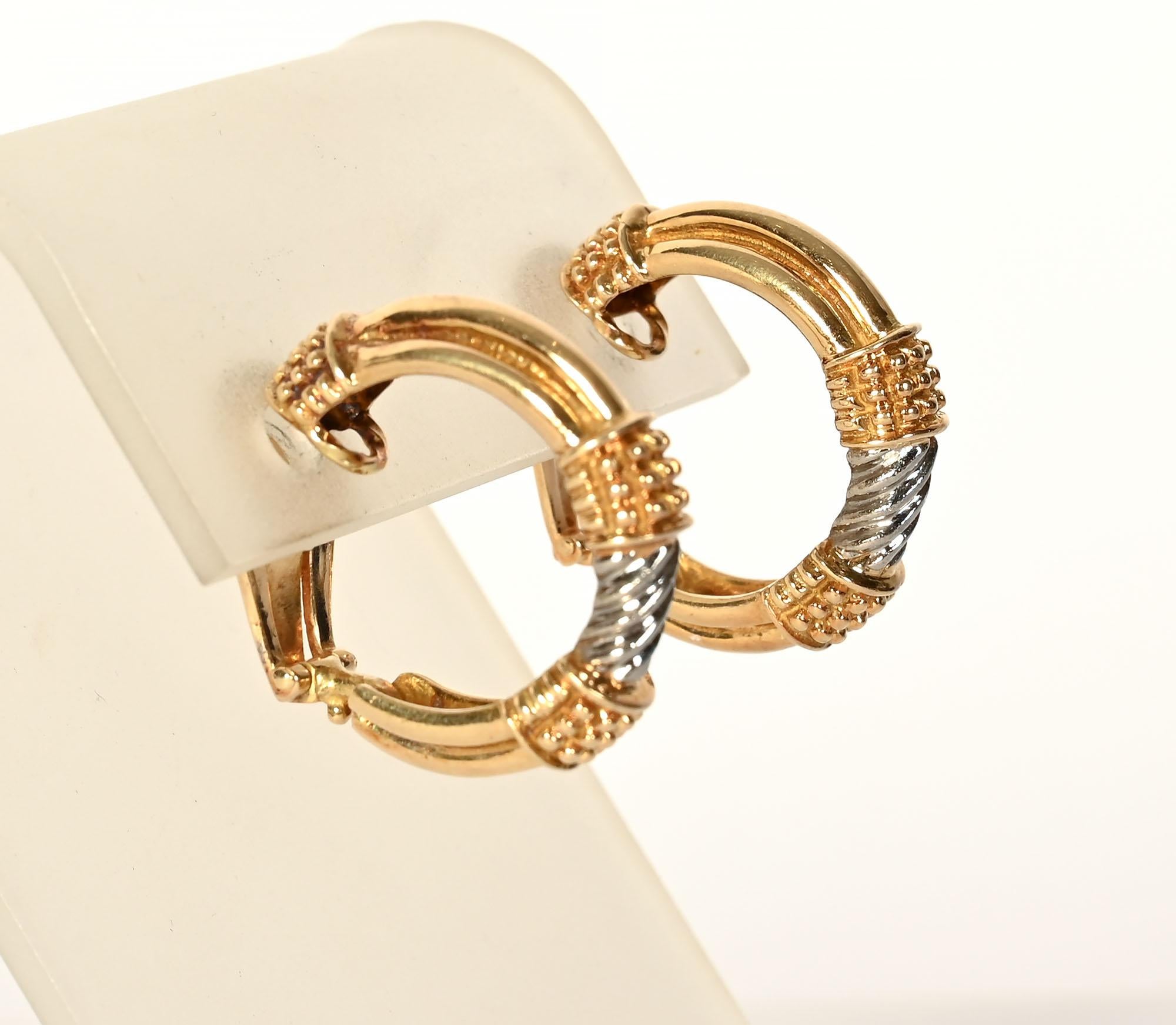 Two features add interest  to these hoop earring by Zolotas. They are both yellow and white gold and have two different textures. The white gold centers have a ribbed, swirl design. On either side of the white gold are small raised balls. They