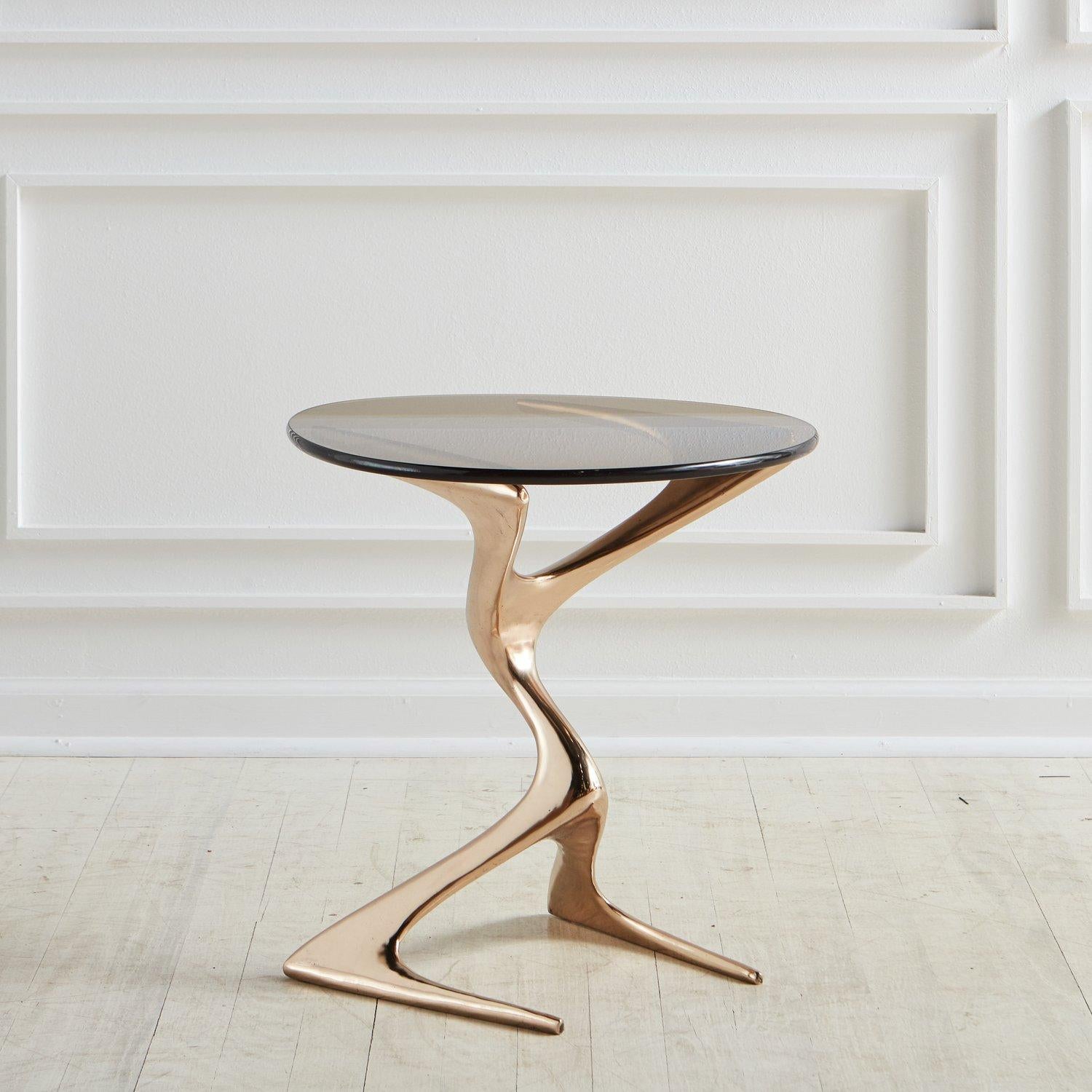 A Zora side table by Chicago artist Karl Geckler in polished bronze with a guitar-pick shaped bronze tinted glass top. Alternative finishes available. Inquire for details.

Karl Geckler works as an interdisciplinary sculptor, architect, and designer