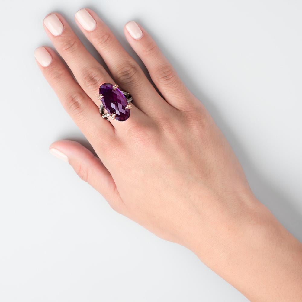 Set with a 22.80 carat dark and undulating amethyst quartz stone, this regal ring is thoroughly magnificent and majestic. This elegant and distinctive mauve gem is nestled into a 0.75 carats white diamond encrusted setting with an ornate split sided