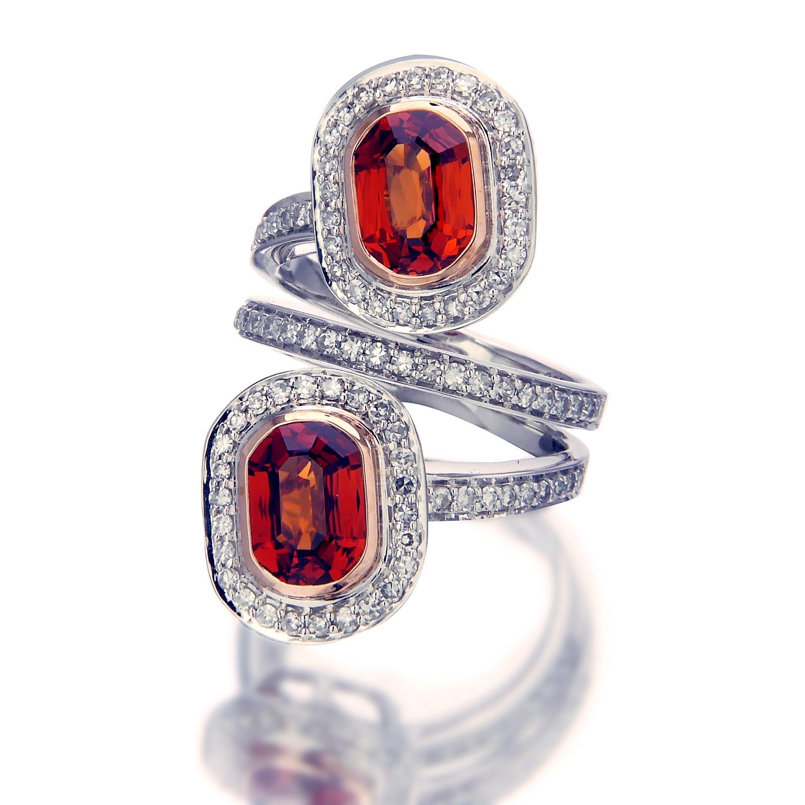 Two reddish-orange spessartite garnets totaling 4.57 carats fixed on pedestals gives this ring a fiery glow. The gems are framed with a row of 0.81-carat diamond pavé that continue down through the circular base of the 18k white gold and palladium