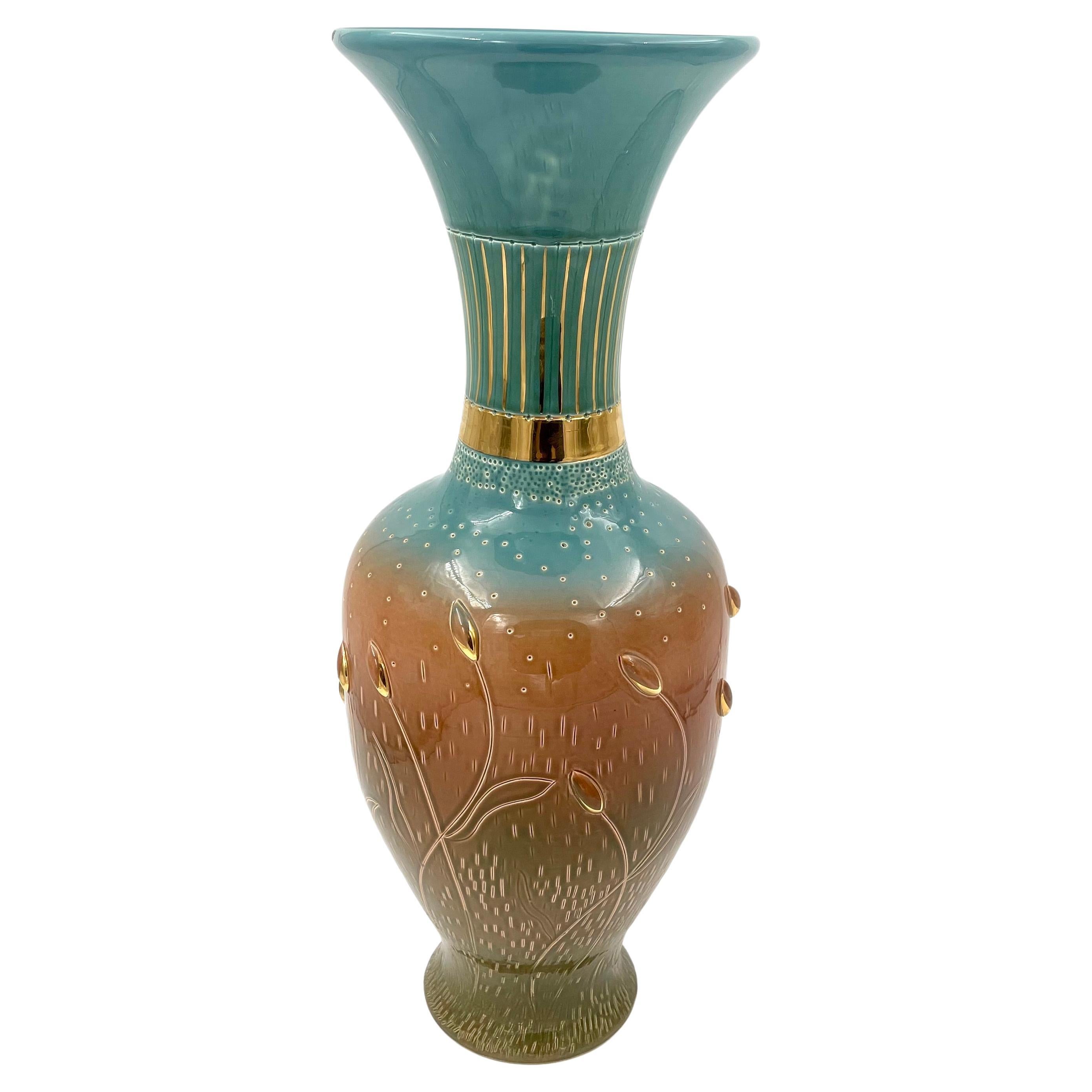 This is a stunning floor vase from the Zsolnay Manufacture's 150th Anniversary collection, designed by artist Edit Bukran. The vase features a striking two-toned color scheme, with gold painting and intricate 3D sculptural elements. It also boasts a