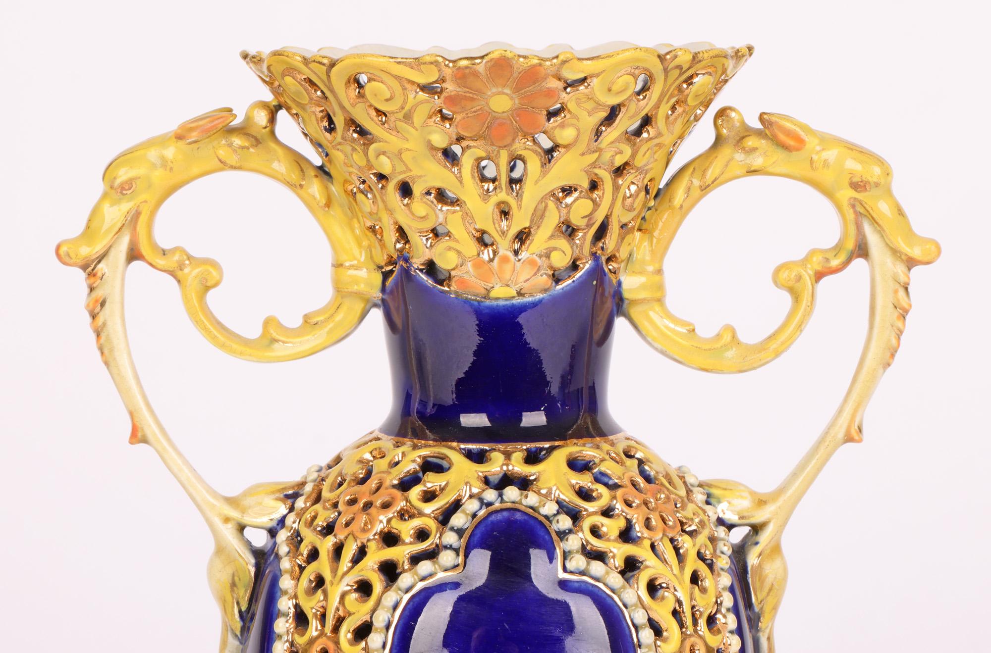 Très beau et élégant vase à deux anses en porcelaine hongroise, avec des motifs floraux réticulés et des panneaux contrastés en glaçure bleue, réalisé par le célèbre fabricant Zsolnay et datant d'environ 1890. Le vase repose sur un pied rond en