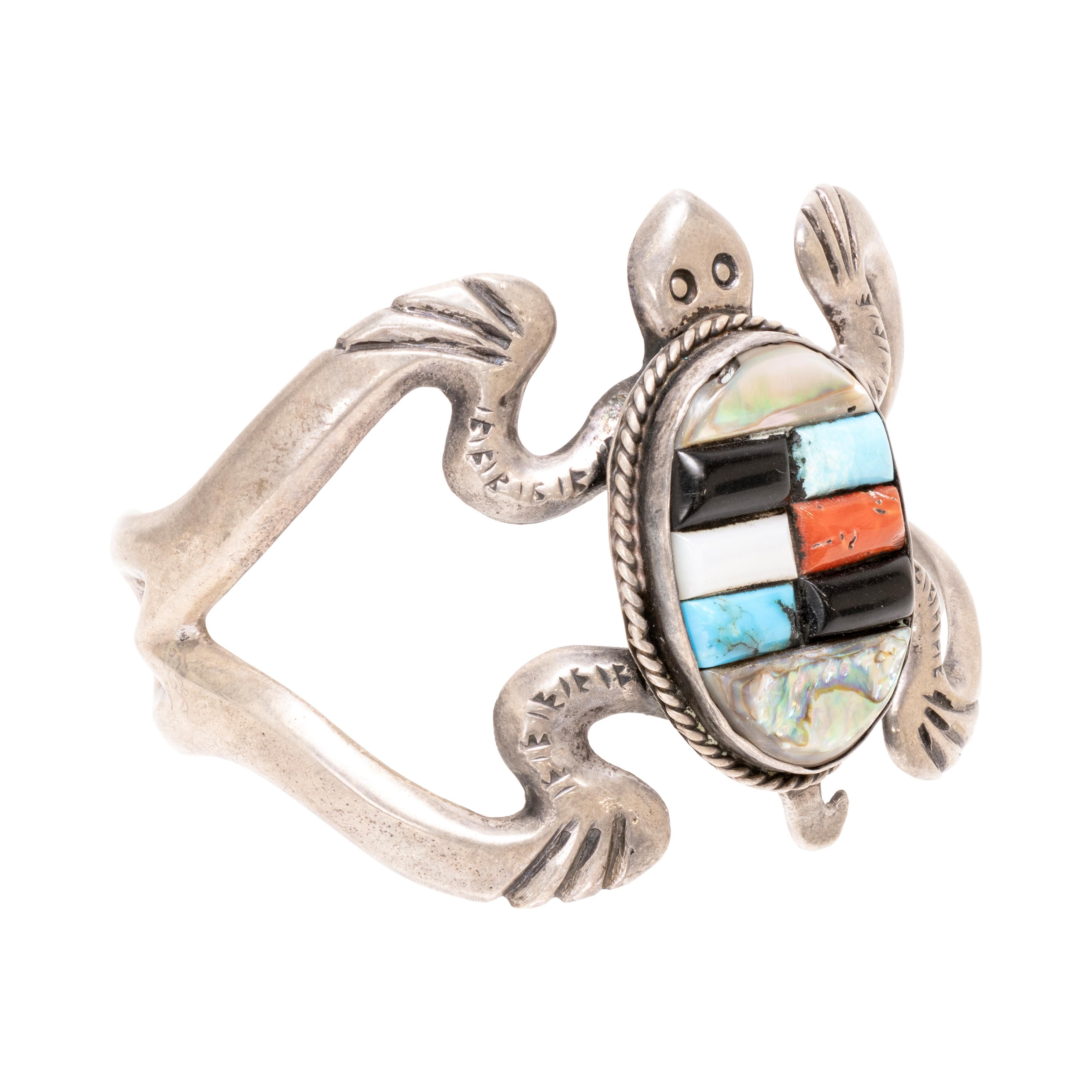 This figurative sand cast bracelet depicts a turtle with a multi-colored shell. The turtle's shell is composed of mother of pearl, turquoise, and coral. The turquoise is from the Kingman Mine in Arizona. Old Pawn. Beautiful, traditional style piece