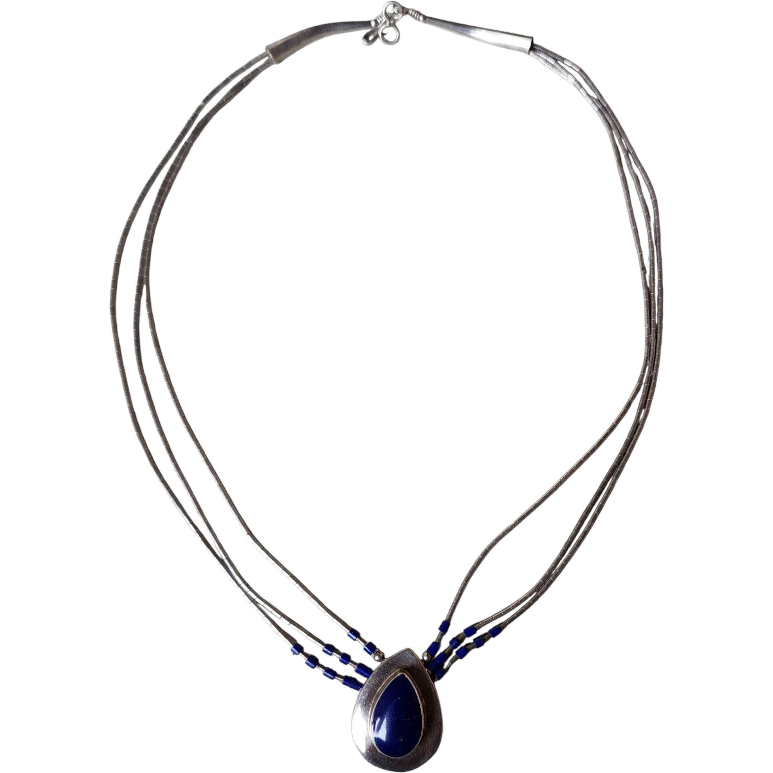 Una straordinaria collana vintage di Zuni fatta a mano, con un design a più fili realizzato con perline tubolari in argento sterling accentate con perline di semi blu reale. Il centro è costituito da un cabochon a goccia di lapislazzuli
