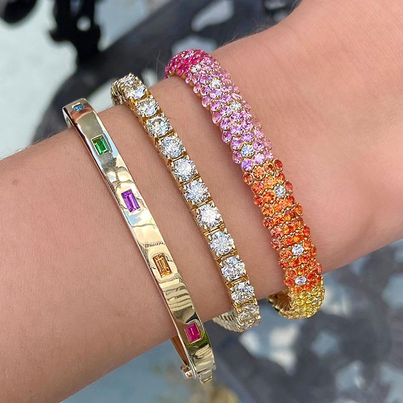 This gorgeous 18kt yellow gold stretch bracelet features 10.52cts of beautiful multicolored sapphires and 1.80cts of vibrant tsavorites, accentuated by 0.75cts of sparkling round diamonds, to create a colorful and eye-catching look. The expanding